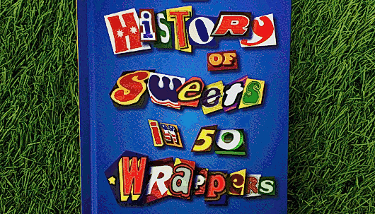 The cover of a blue book, with the title 'History of sweets in 50 wrappers' spelt out in colourful cut-out letters. The book is against a green background