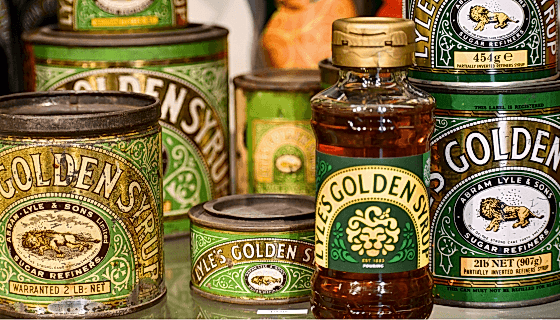 A selection of old green and gold Lyle's Golden Syrup tins, with one new plastic Lyle's Golden Syrup bottle at the front